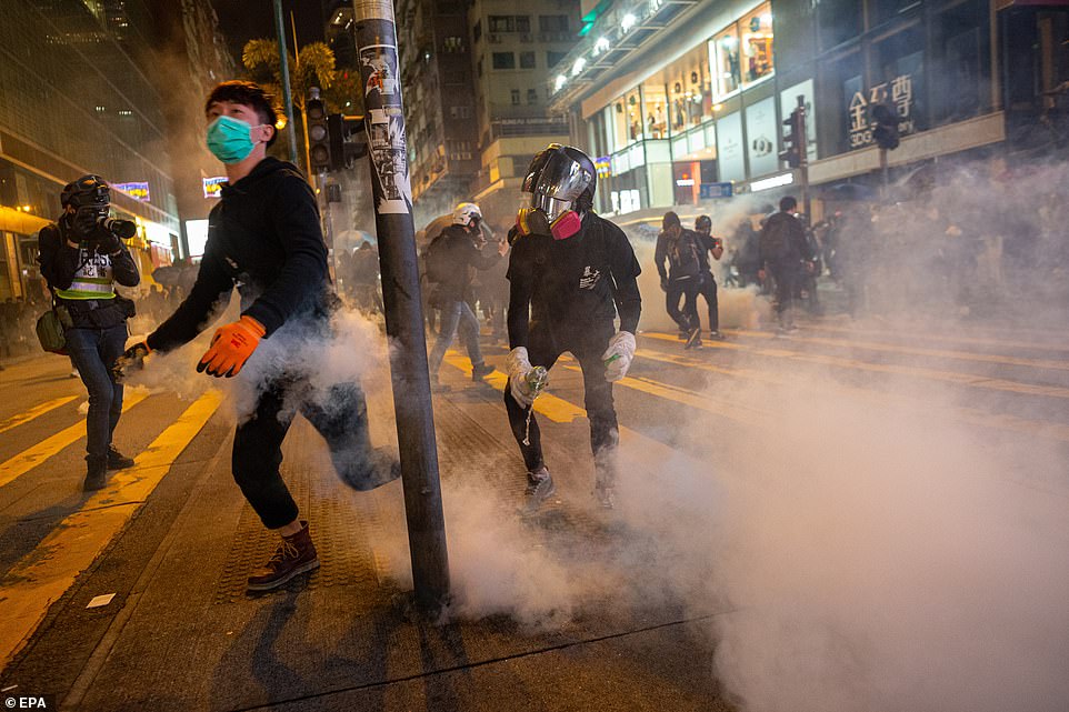 Protesters wearing masks across the faces run away from police as tear gas floods onto the streets on Christmas Eve