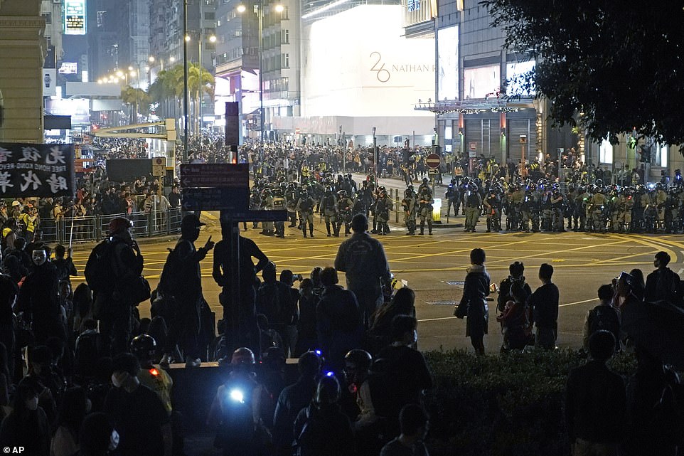 Riot police holding shields against their chest congregate on a street in Hong Kong and confront hundreds of protesters during a rally