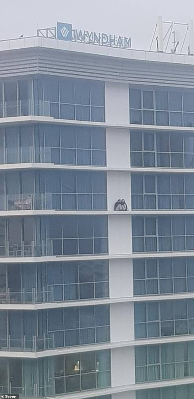 A couple have bizarrely climbed over a 14th floor balcony on the Gold Coast to sit on the ledge of the building and have a chat