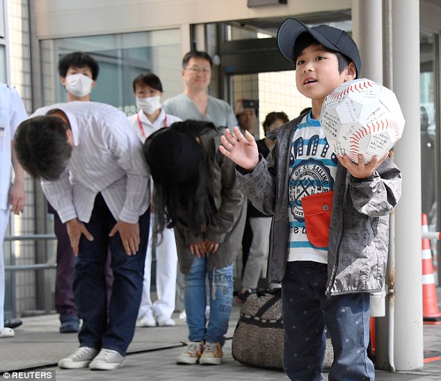 Seven-year-old Yamato Tanooka has been pictured smiling and waving on his release from hospital as his parents stand behind him bowing in apology (pictured) 