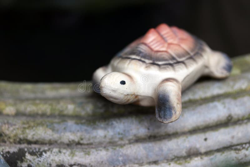 Baked clay of turtle put decorate on the edge of cement pot. Turtle pottery on the edge of pot and black background royalty free stock image