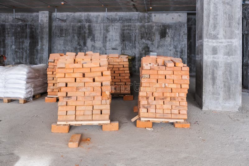 Pallets with red clay brick and bags of cement at a construction site inside a house. Under construction stock photos