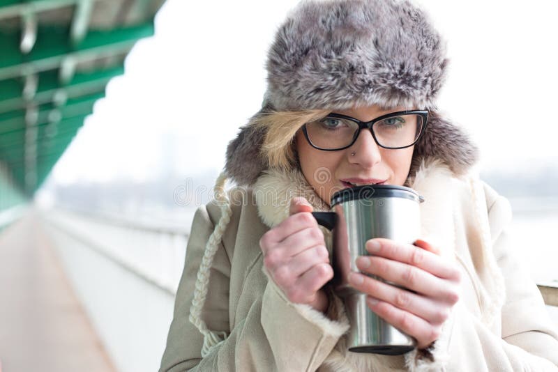 Portrait of woman drinking coffee from insulated drink container during winter stock image