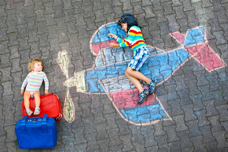 Two little children, kid boy and toddler girl having fun with with airplane picture drawing with colorful chalks on stock photo